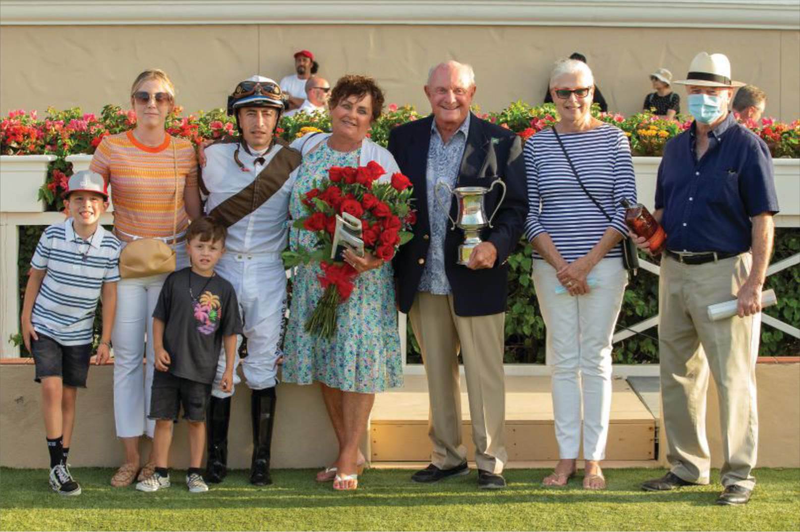 A family standing with jockey, wife holding a bouquet of roses, husband holding a trophy